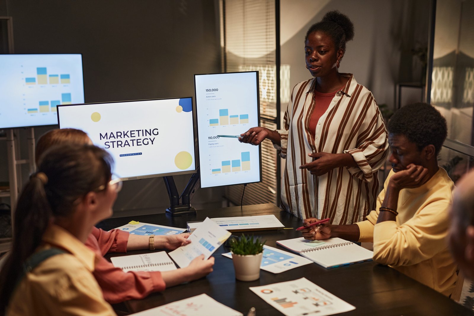 Portrait of young black woman giving presentation on marketing to team in dimly lit office