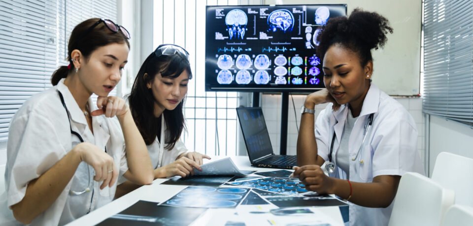 Team of female doctor check on scan results paper and looking at monitors in laboratory and plan and share medical knowledge and experience benefits her coworkers and patients