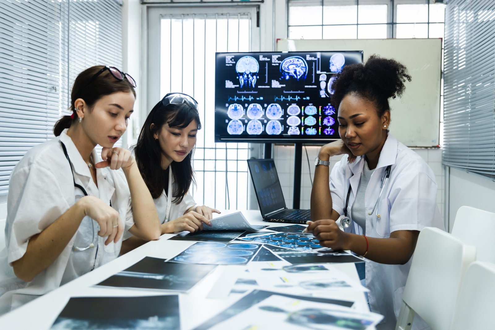 Team of female doctor check on scan results paper and looking at monitors in laboratory and plan and share medical knowledge and experience benefits her coworkers and patients