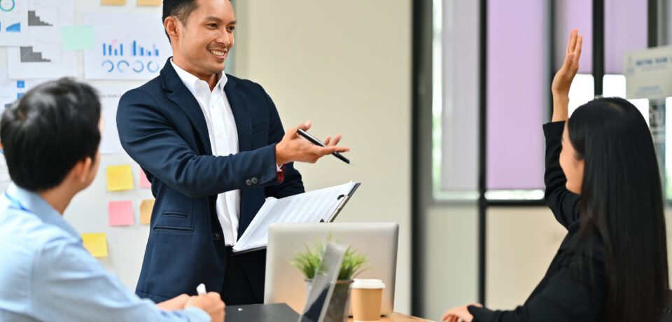 Businesswoman raising hand, asking question during her colleagues presentation at meeting. How to Develop a B2B Content Strategy That Turns Leads into Devoted Customers