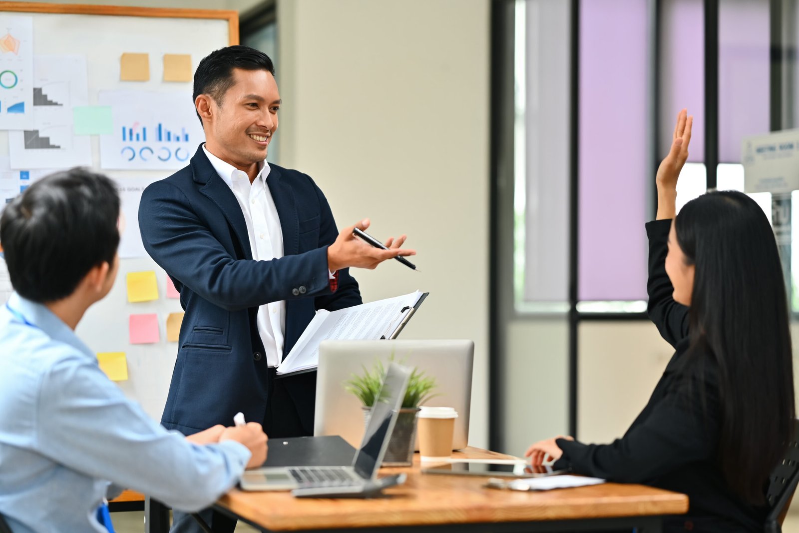Businesswoman raising hand, asking question during her colleagues presentation at meeting