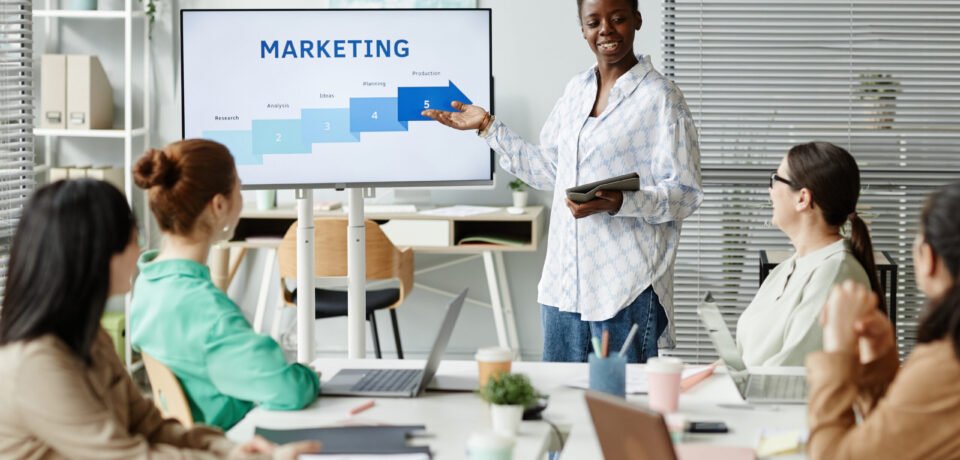 African young businesswoman pointing at monitor and presenting her report to colleagues at business presentation at office