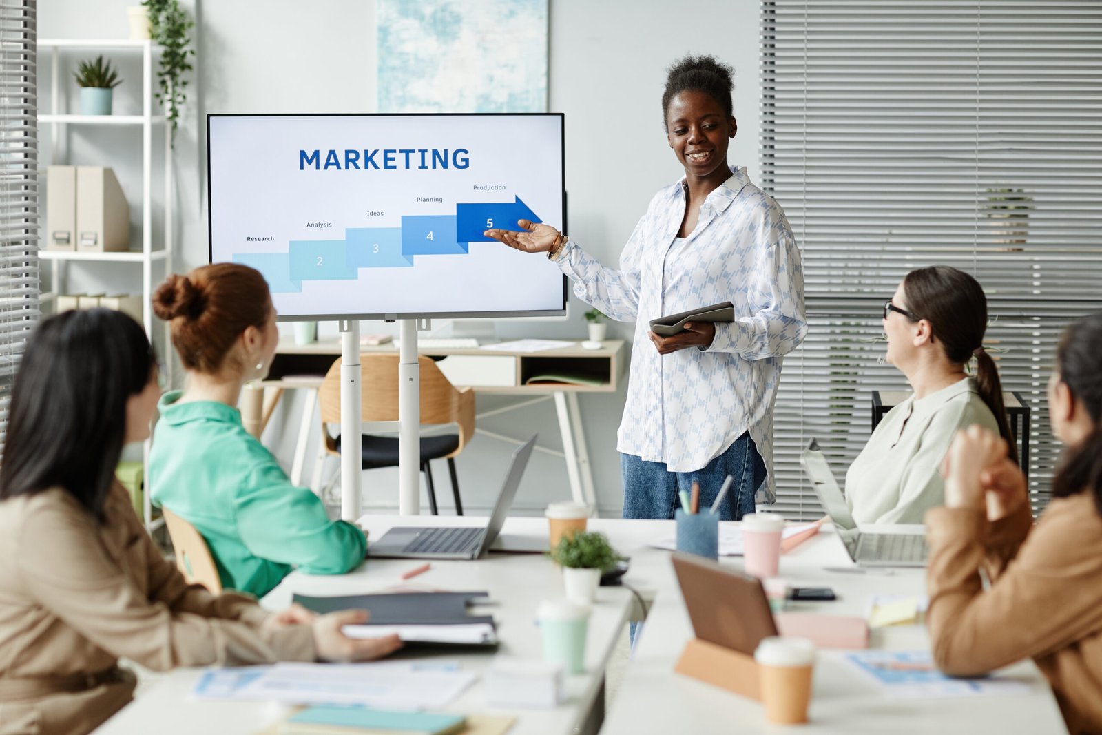 African young businesswoman pointing at monitor and presenting her report to colleagues at business presentation at office