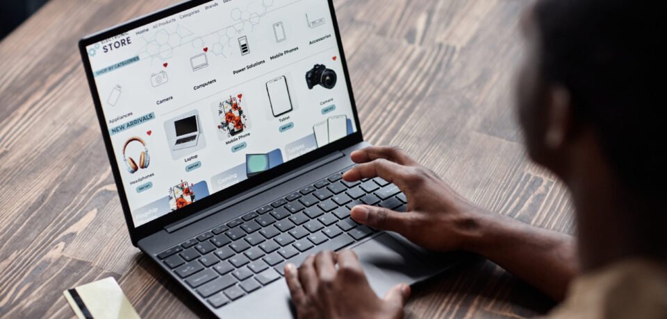 High angle view of unrecognizable Black man sitting at wooden desk choosing goods in online shop on laptop