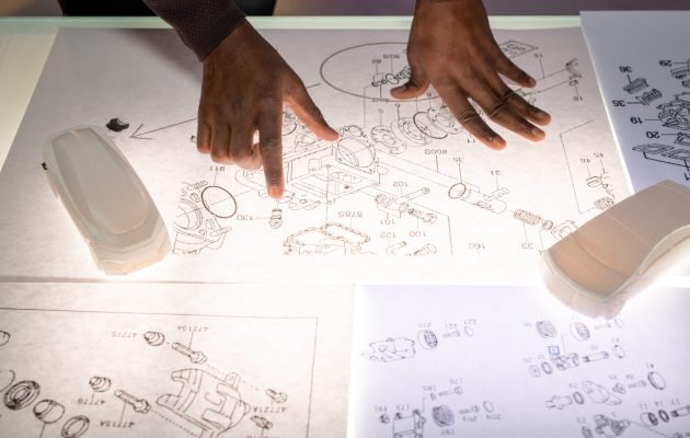Automotive engineer analyzing sketches Above view of black automotive engineer standing at desk with car models and analyzing sketches