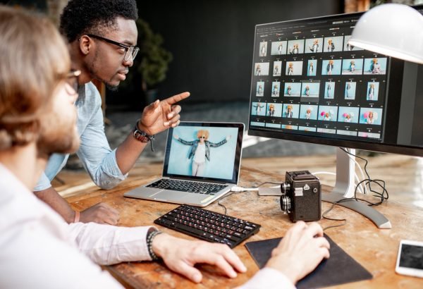 Two photographers working on the computers in the studio Two male photographers choosing woman's portraits at the working place with two computers in the studio